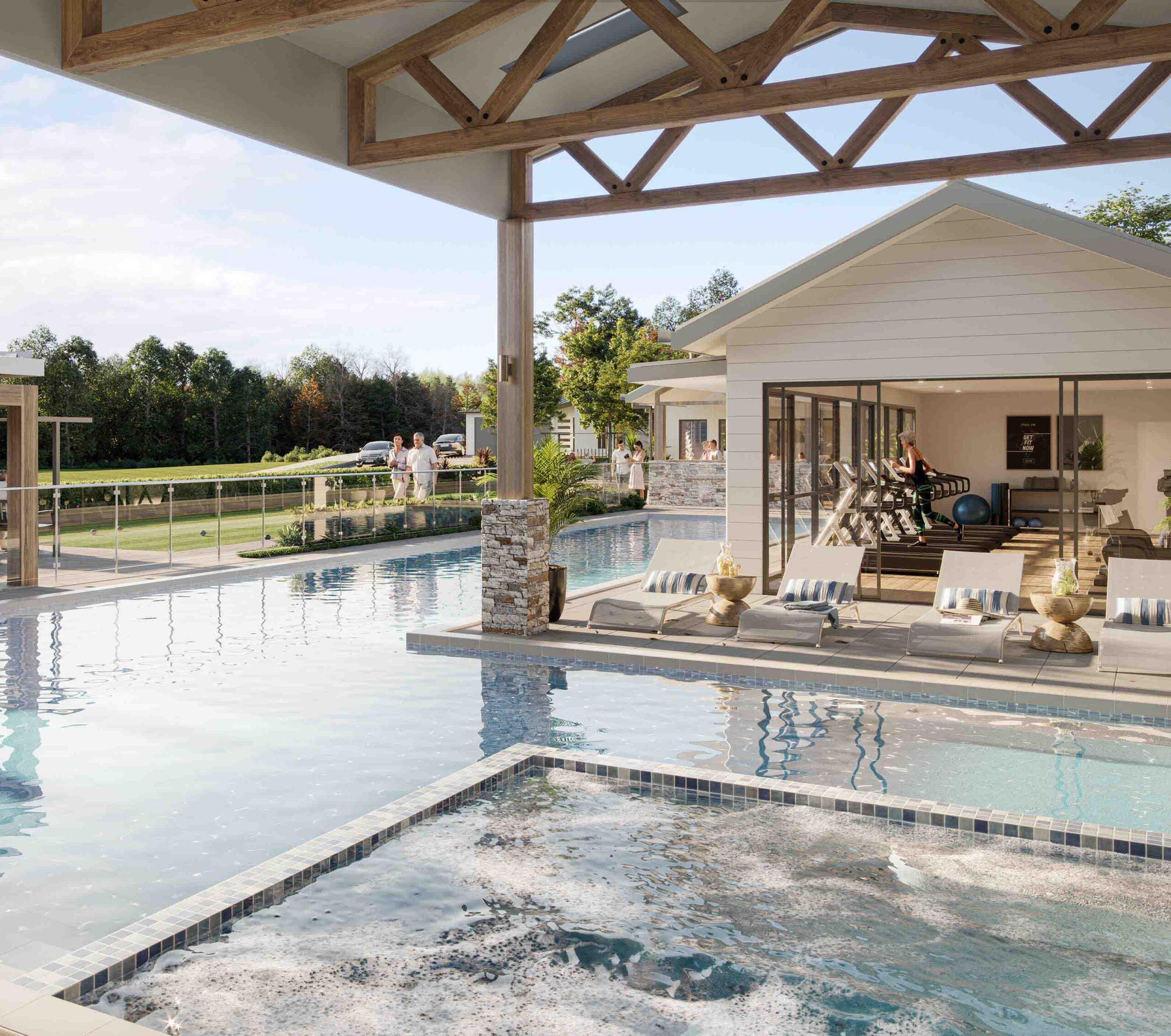 Lifestyle village swimming pool with hot tub within modern open-air structure, people relaxing on lounge chairs nearby, surrounded by greenery and sunny sky.