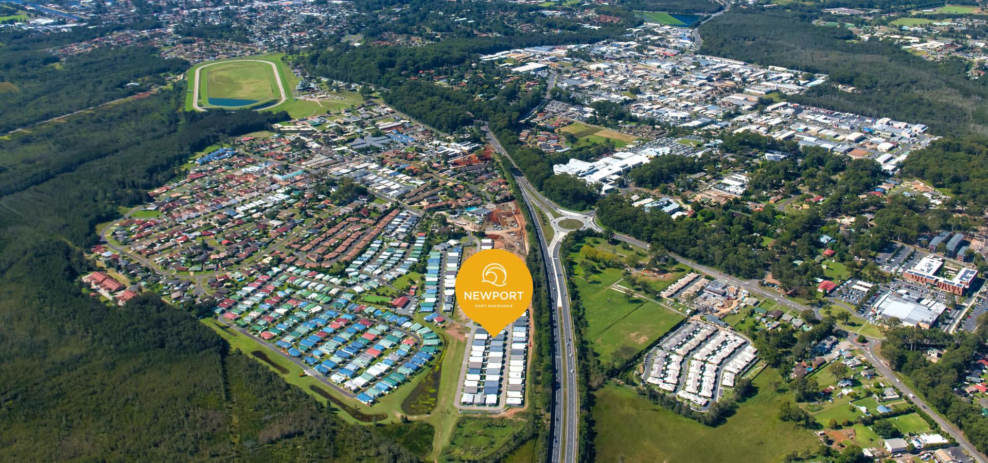 Aerial view of a suburban area with densely arranged lifestyle village houses, a sports field, roads, green spaces, and vegetation. "Newport" logo present.