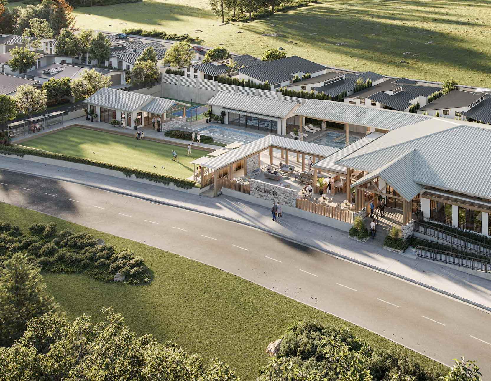 Modern lifestyle village building complex with people socializing on a grassy area in front, set against trees and a road in a serene community environment.
